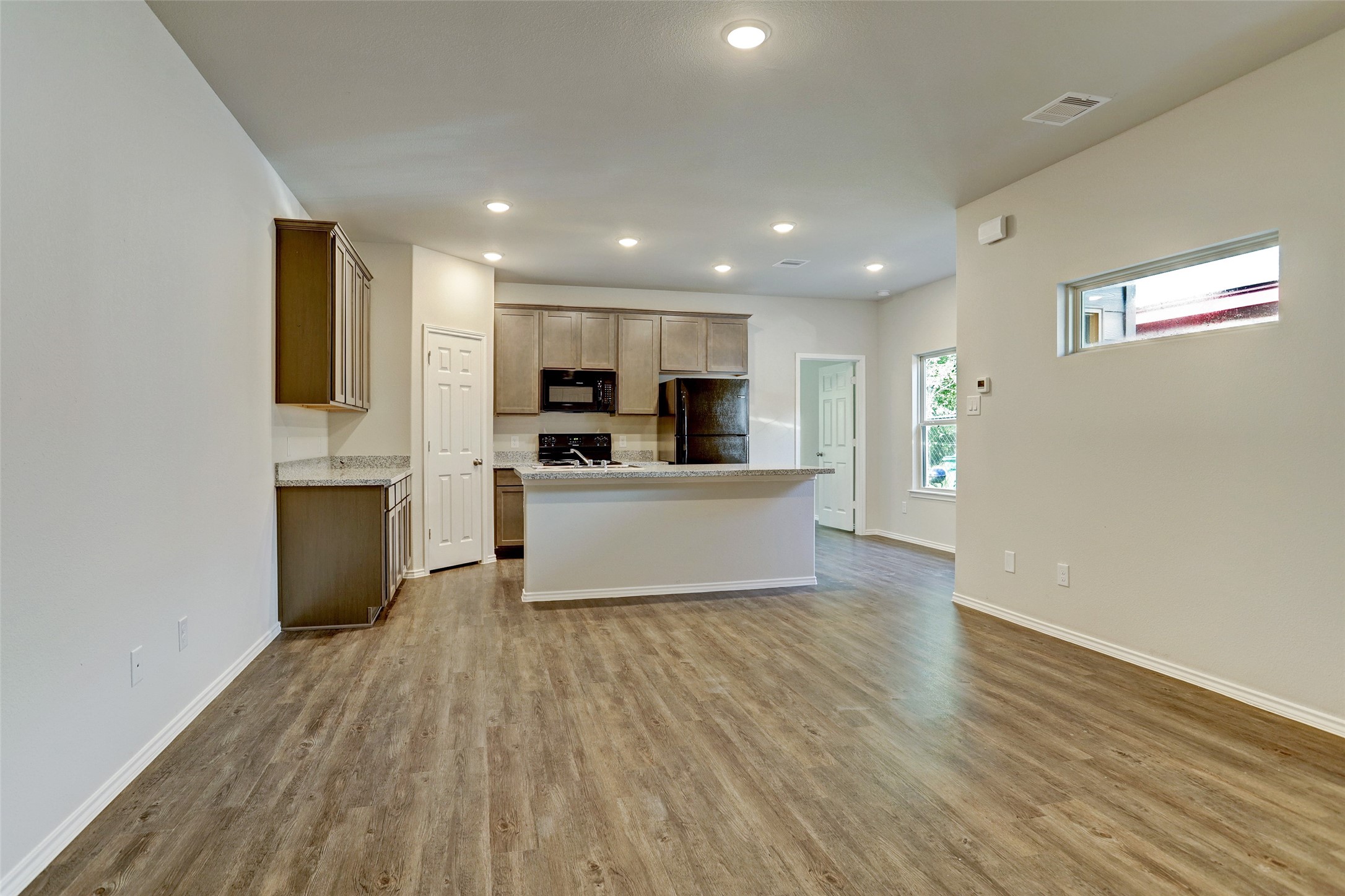409 South 12th Street, Unit B Conroe, TX 77301 - Photo 4 of 14 This photo showcases a modern, open-concept kitchen and living area with wood-style flooring, recessed lighting, and neutral walls. The kitchen features granite countertops, ample cabinetry, and a central island, creating an inviting space for cooking and entertaining.