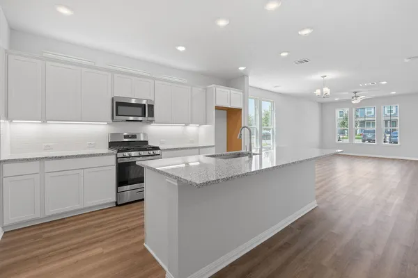 a kitchen with kitchen island granite countertop a stove a sink a refrigerator and white cabinets with wooden floor