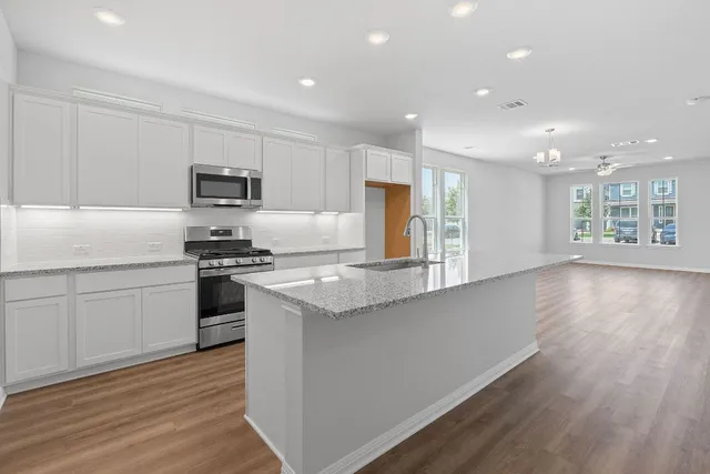 a kitchen with kitchen island granite countertop a stove a sink a refrigerator and white cabinets with wooden floor