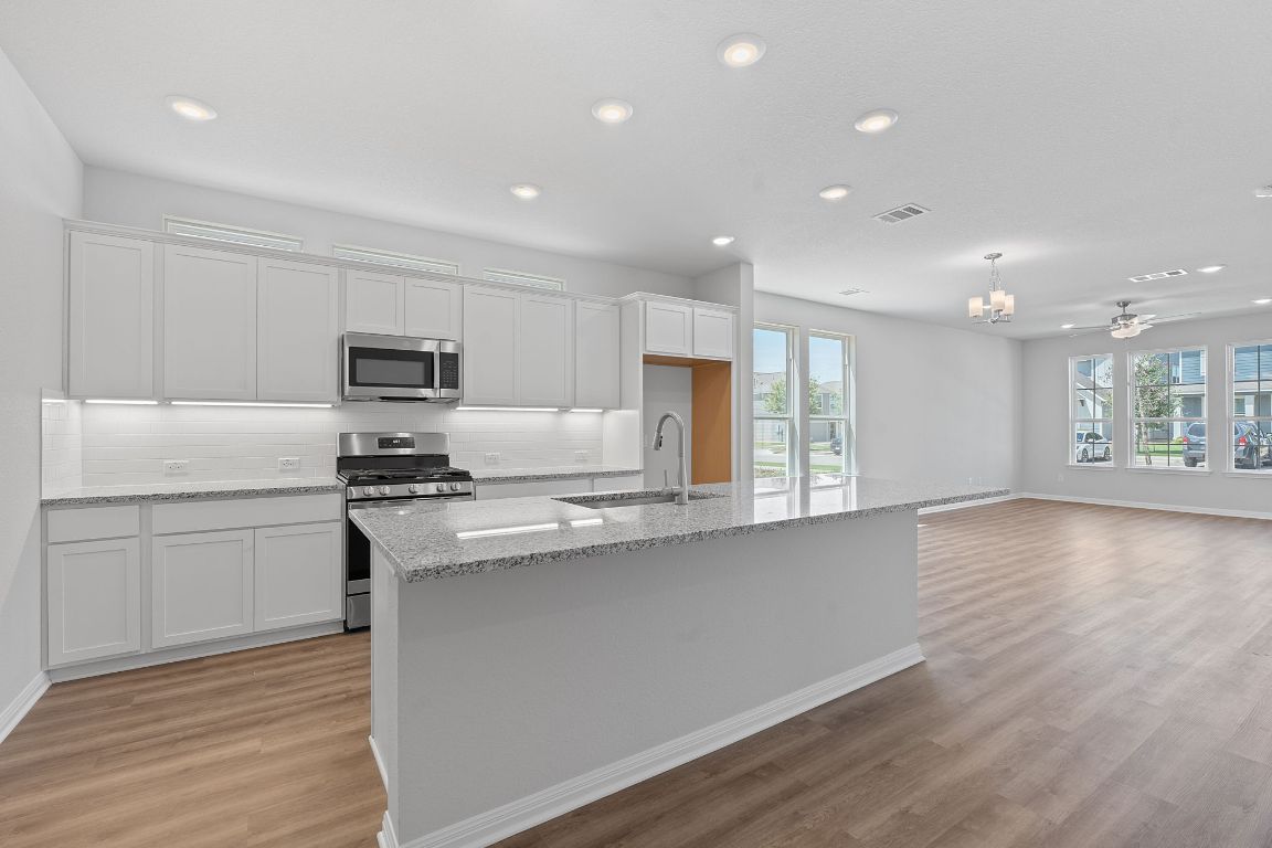 376 Blue Oasis Lane Leander, TX 78641 - Photo 14 of 27 a kitchen with stainless steel appliances granite countertop a sink a stove a refrigerator and white cabinets with wooden floor