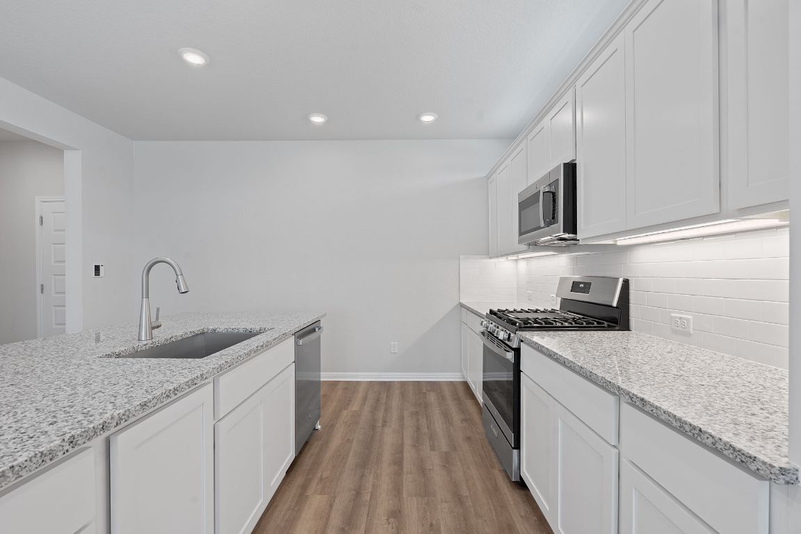 376 Blue Oasis Lane Leander, TX 78641 - Photo 10 of 27 a kitchen with granite countertop a sink stainless steel appliances and white cabinets