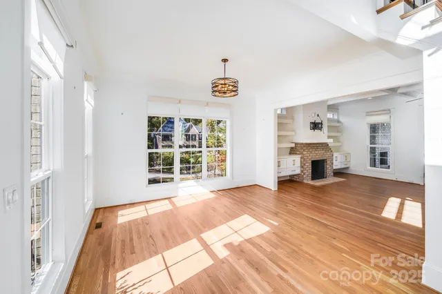 a view of an empty room with wooden floor fireplace and a window