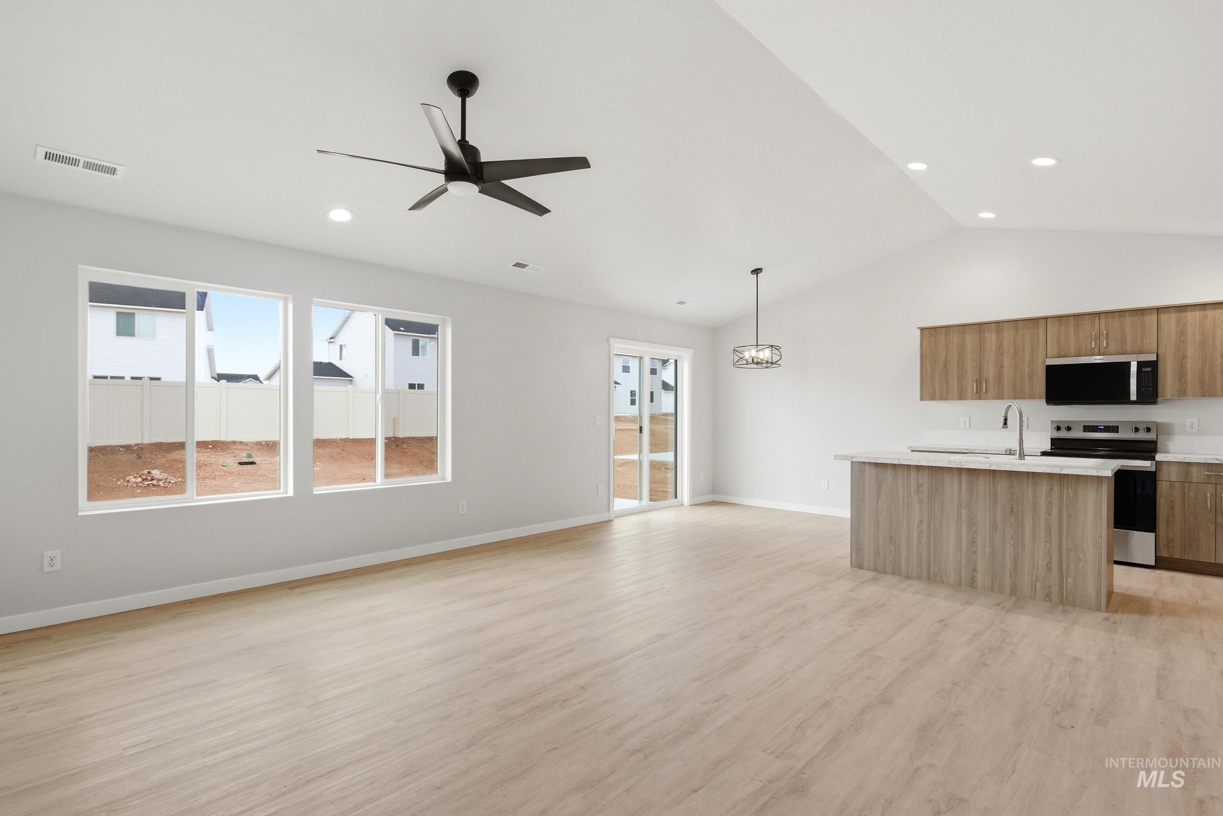 16632 North Shorthorn Loop Nampa, ID 83651 - Photo 10 of 17 Open-concept living area featuring vaulted ceilings, wood-finish flooring, a modern kitchen island with integrated sink, stainless steel appliances, and abundant natural light from large windows and a sliding glass door