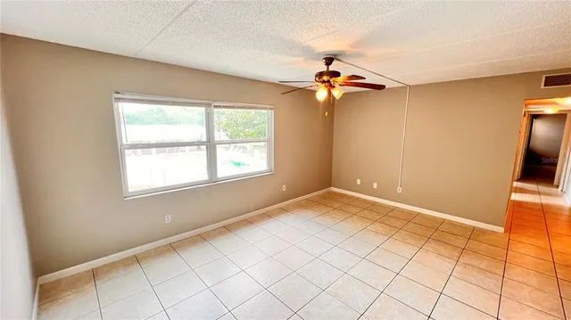 a view of an empty room and chandelier fan and kitchen view