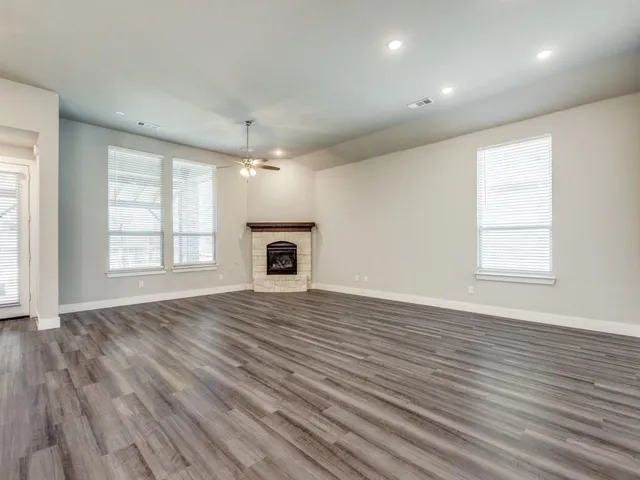 an empty room with wooden floor fireplace and windows