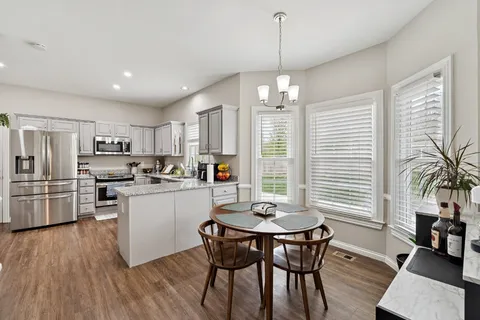 a kitchen with stainless steel appliances kitchen island granite countertop a table chairs refrigerator and microwave