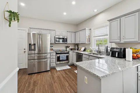 a kitchen with granite countertop a refrigerator a sink dishwasher a stove top oven a refrigerator with wooden floor and cabinets