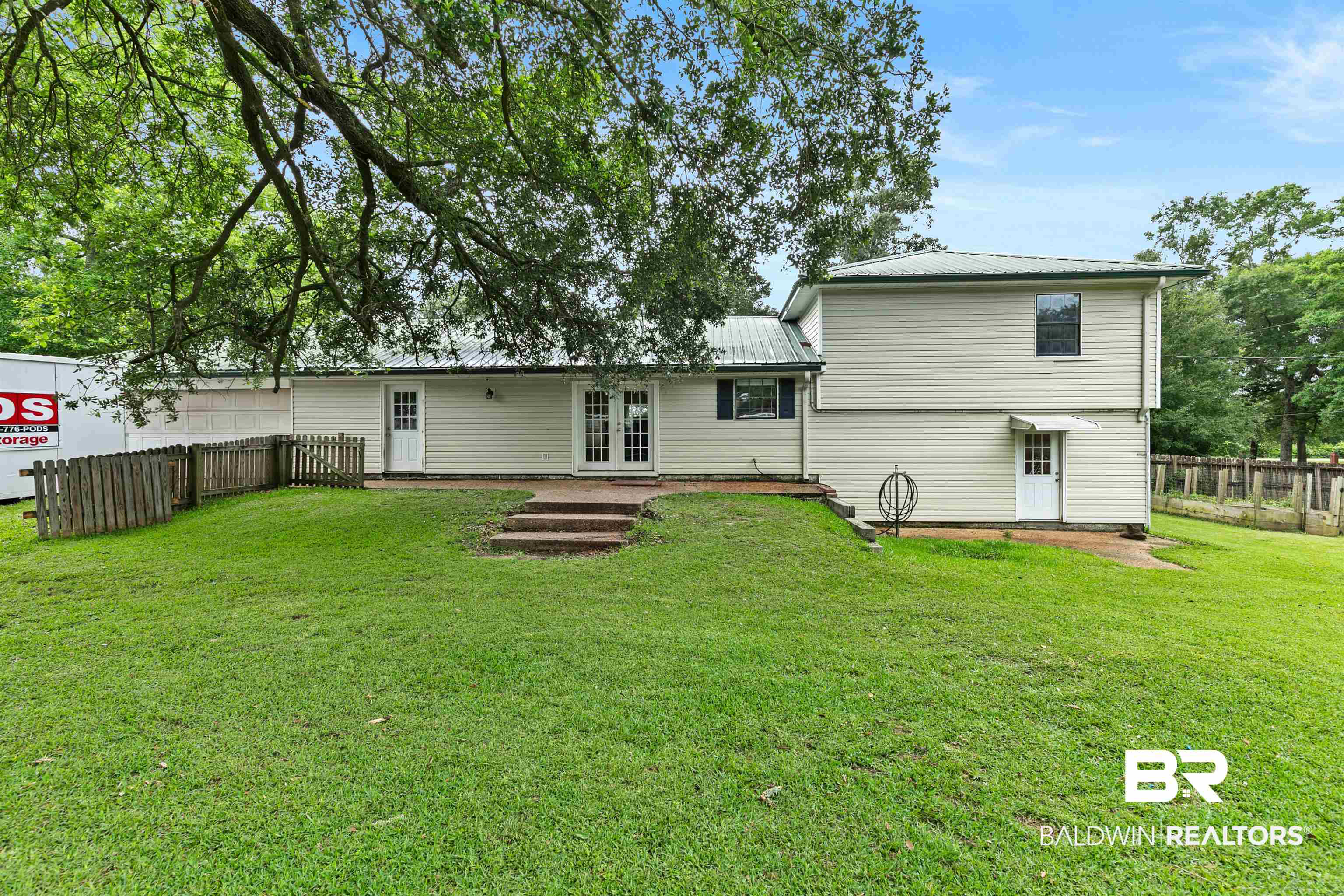 10420 Johnson Road South Mobile, AL 36695 - Photo 50 of 75 Expansive green lawn with mature shade trees, featuring a multi-level house with light-colored siding and a metal roof