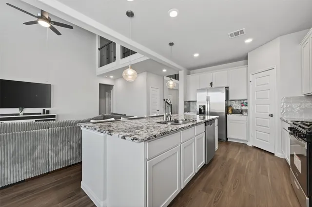 a kitchen with stainless steel appliances granite countertop a stove top oven a refrigerator a sink and dishwasher with wooden floor