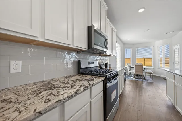 a kitchen with stainless steel appliances granite countertop a stove top oven a sink dishwasher a dining table and chairs with wooden floor