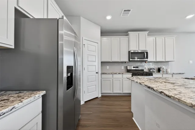 a kitchen with stainless steel appliances granite countertop a refrigerator stove and white cabinets