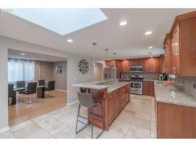 a kitchen with stainless steel appliances granite countertop a stove a sink a refrigerator and chairs