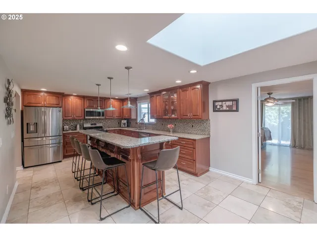 a kitchen with stainless steel appliances kitchen island granite countertop a table chairs sink and refrigerator