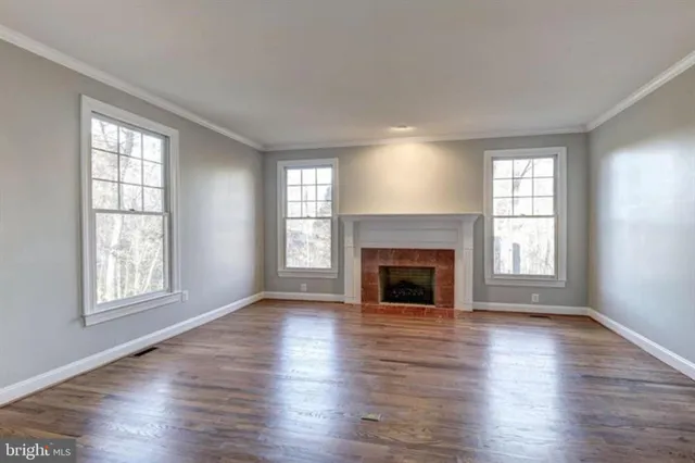 an empty room with wooden floor fireplace and windows