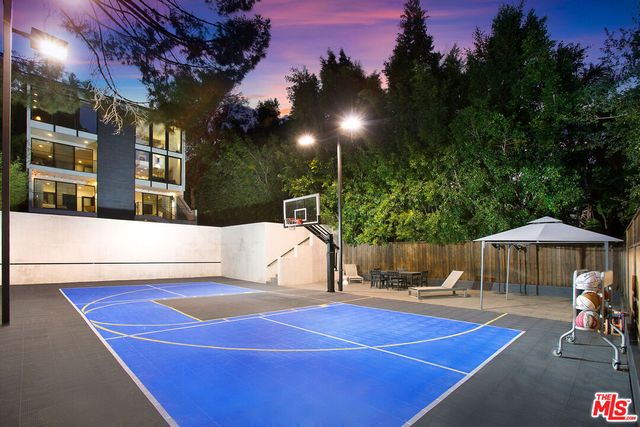 a view of a tennis court with table and chairs under an umbrella with palm trees