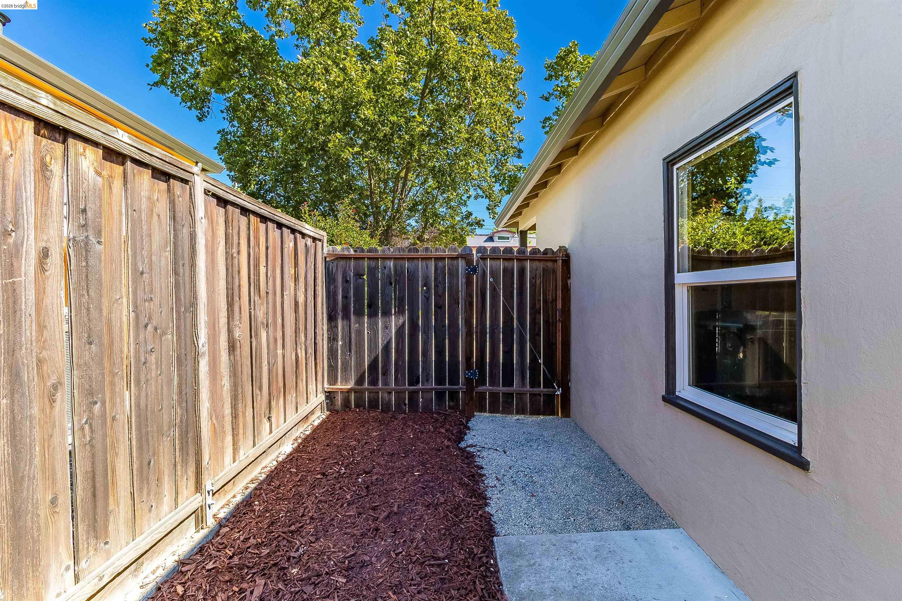 346 Valley View Road Pleasant Hill, CA 94523 - Photo 44 of 57 Side yard with a wood fence, a gravel and concrete path, and a window with dark trim on a stucco exterior