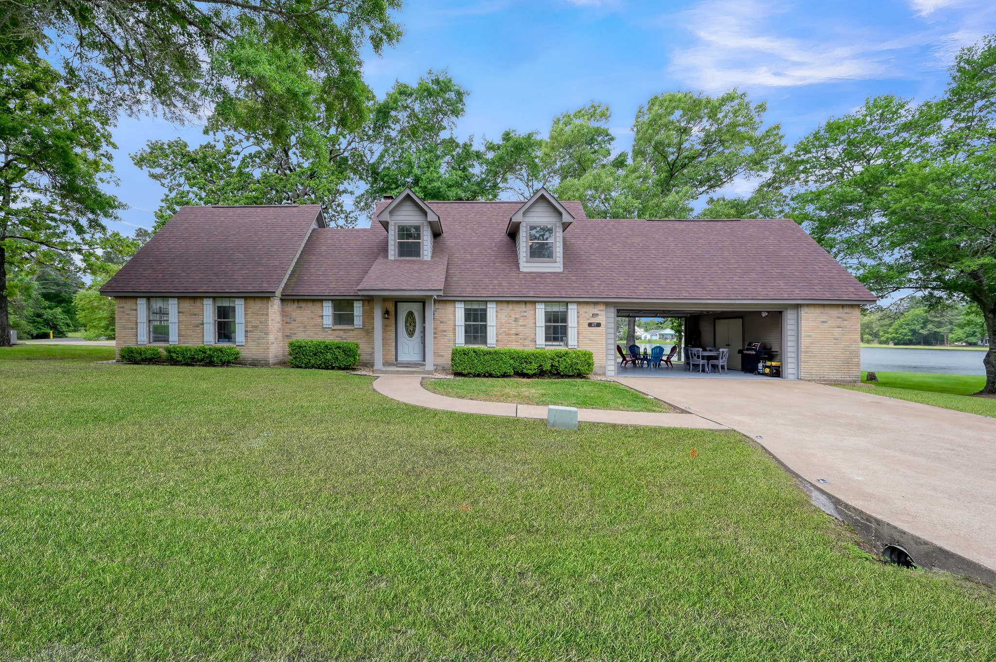 117 Brookside Drive Trinity, TX 75862 - Photo 8 of 46 Front elevation of a two-story brick home with an upper level featuring two dormer bedrooms. The garage is a pass-through with front and back garage doors, showcasing a beautiful lake view.