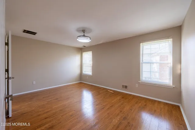 an empty room with wooden floor fan and windows