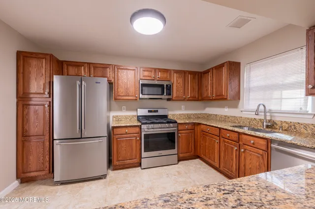 a kitchen with stainless steel appliances granite countertop a stove top oven a refrigerator and a sink with wooden cabinets