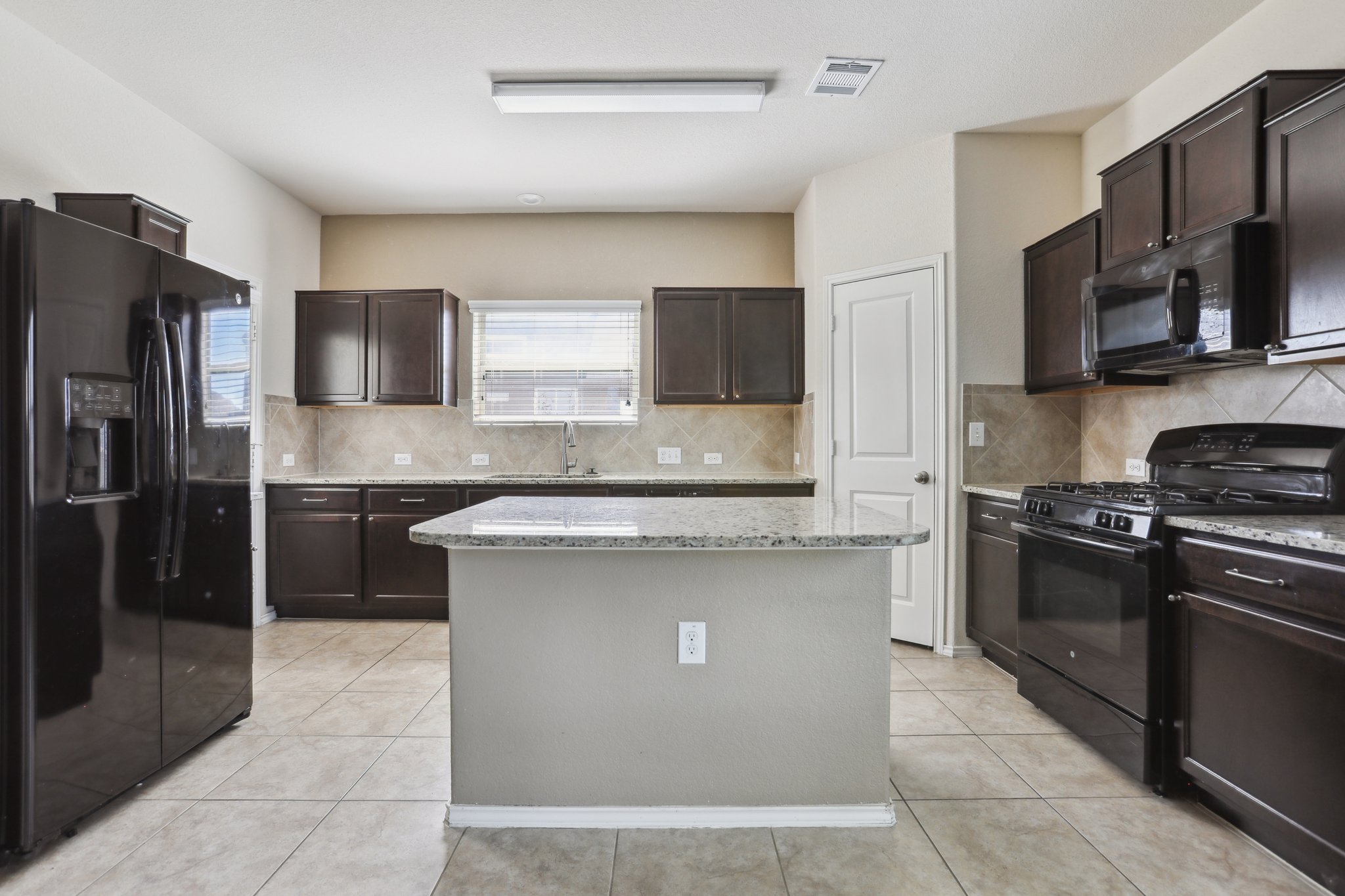 5713 Kennedy Street Austin, TX 78747 - Photo 2 of 30 Kitchen featuring black appliances, dark wood finish cabinets, a kitchen island, light stone counters, and light tile patterned floors