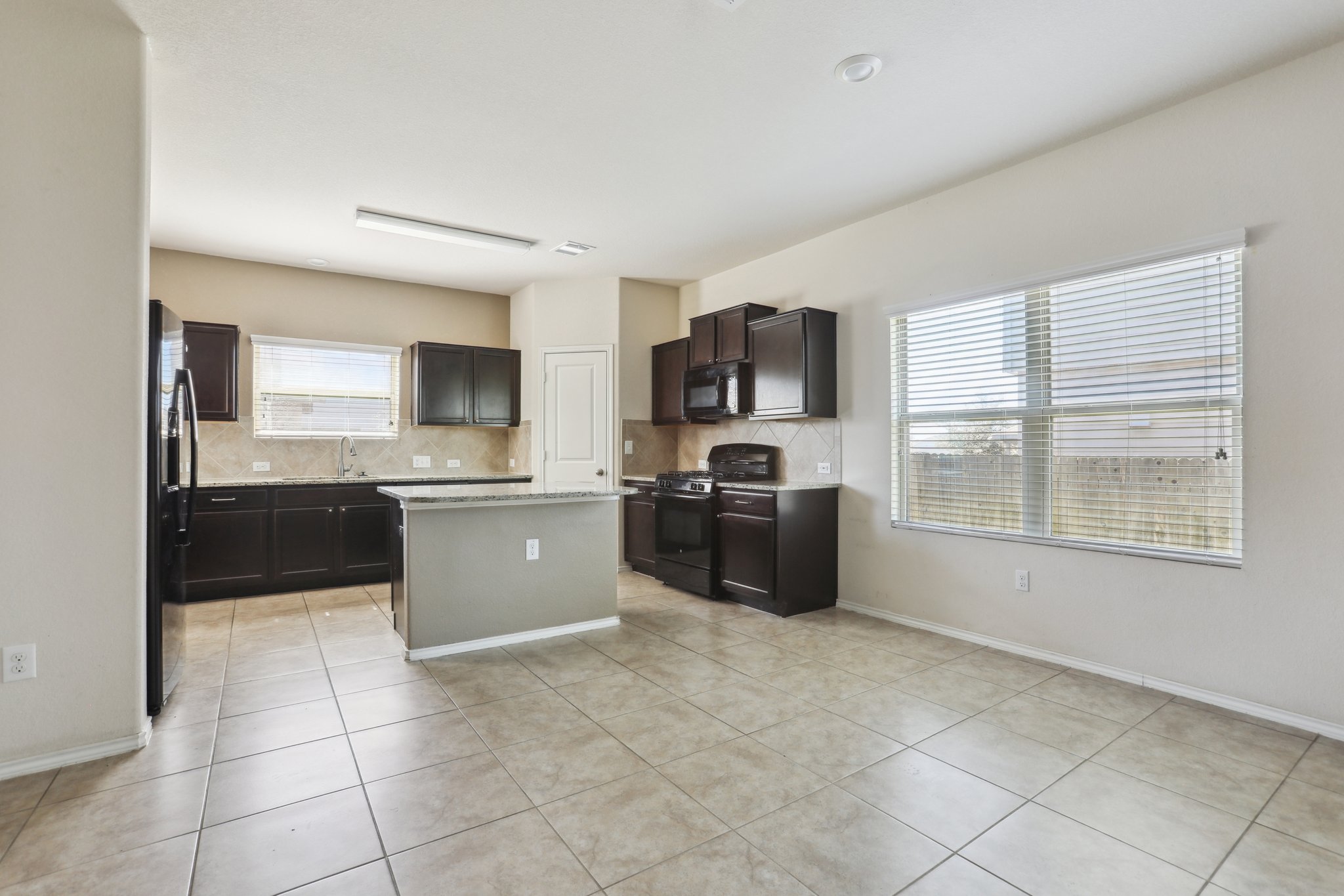 5713 Kennedy Street Austin, TX 78747 - Photo 3 of 30 Kitchen featuring black appliances, decorative backsplash, a center island, dark wood finish cabinets, and light tile patterned floors