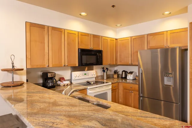 a kitchen with granite countertop a refrigerator a sink a stove top oven and cabinets