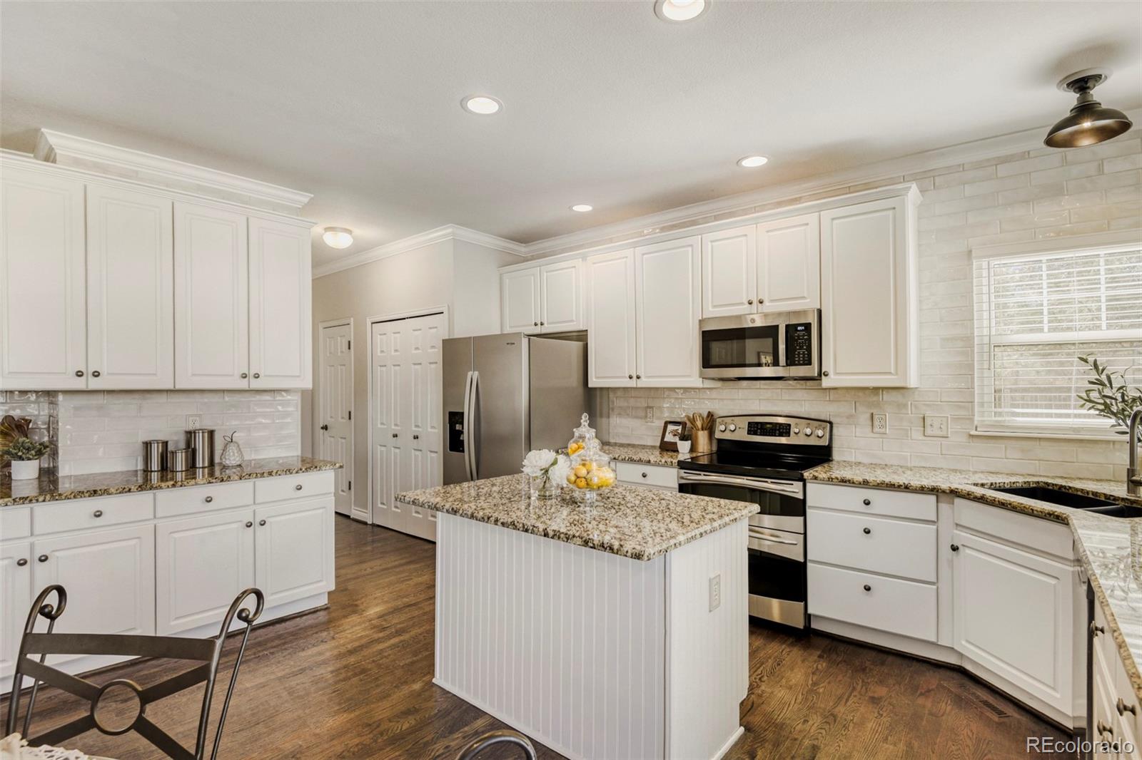 8573 South Mallard Court Highlands Ranch, CO 80126 - Photo 11 of 50 a kitchen with stainless steel appliances granite countertop a sink stove refrigerator and white cabinets with wooden floor