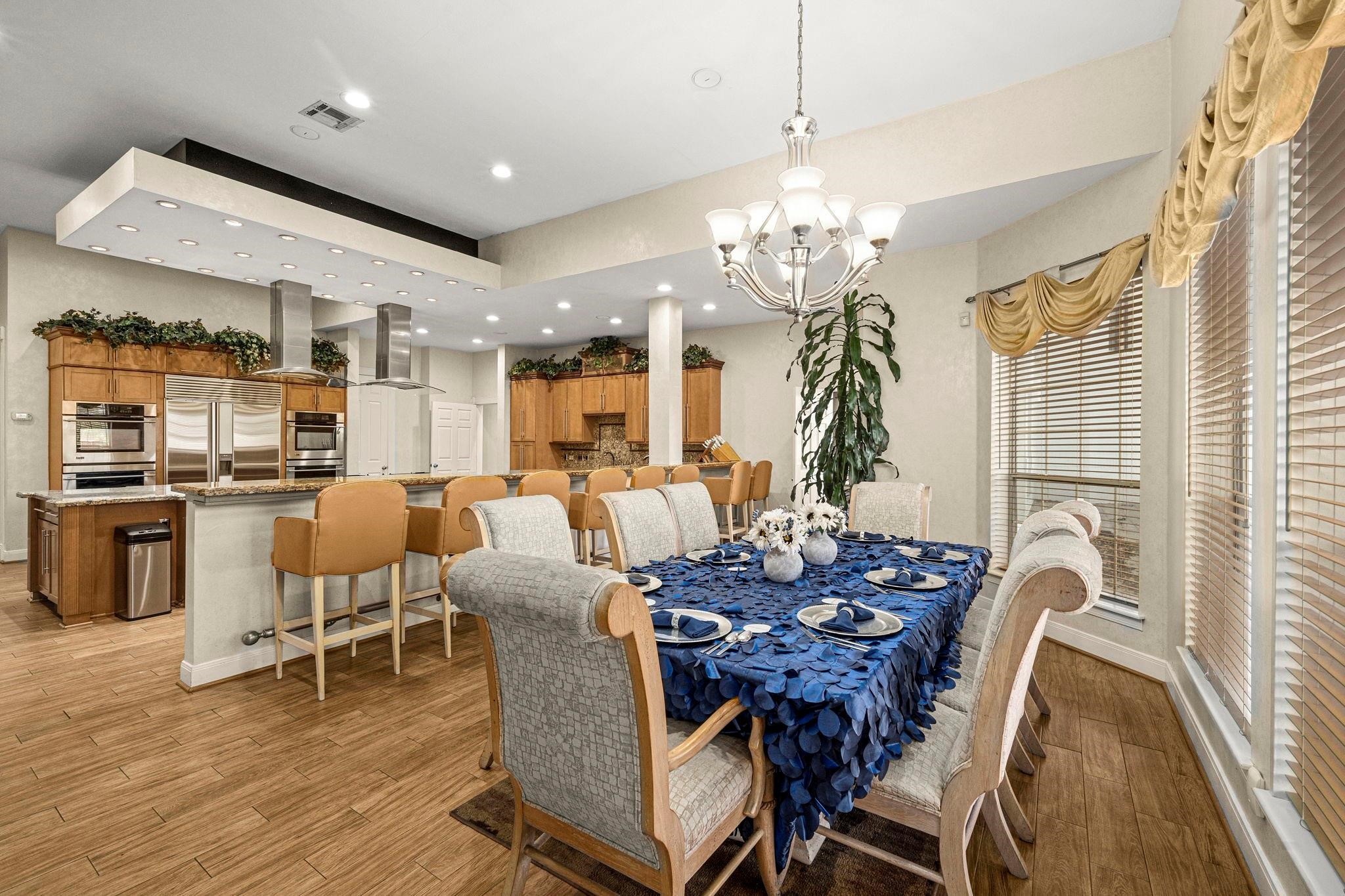 19525 Doerre Road Spring, TX 77379 - Photo 11 of 39 This photo showcases a spacious, open-concept dining and kitchen area with modern appliances, ample cabinetry, and elegant lighting. The breakfast space features a large table set for entertaining, complemented by a sophisticated chandelier. The room is well-lit and inviting, with a warm color palette and hardwood flooring.