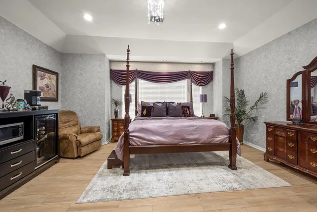 a bedroom with a bed a dresser and potted plants with the wooden floor