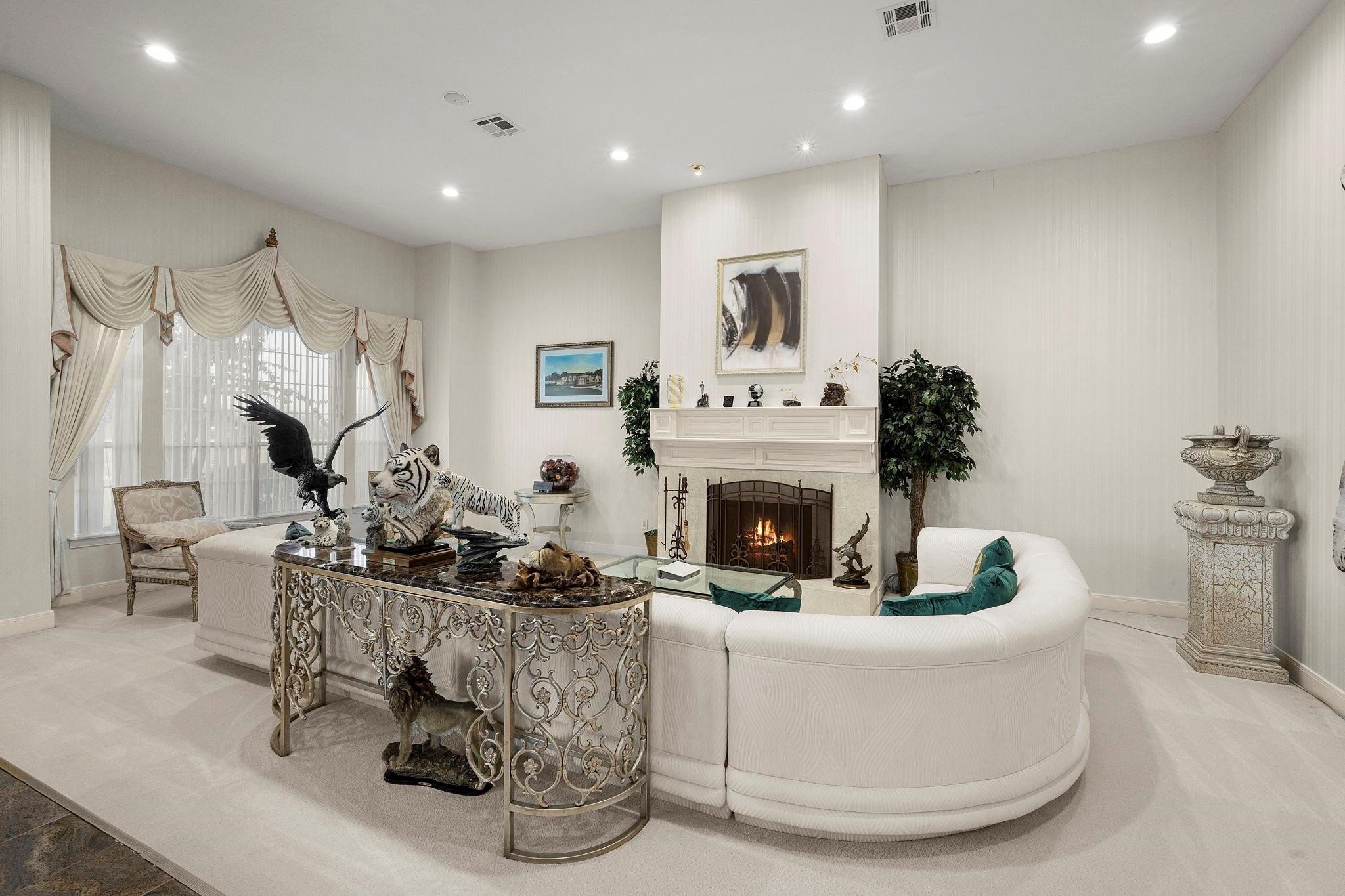 19525 Doerre Road Spring, TX 77379 - Photo 6 of 39 This is an elegantly furnished living room featuring a cozy fireplace, large windows with decorative curtains, and a mix of classical and eclectic decor. The room has a light and airy feel, with a neutral color palette.