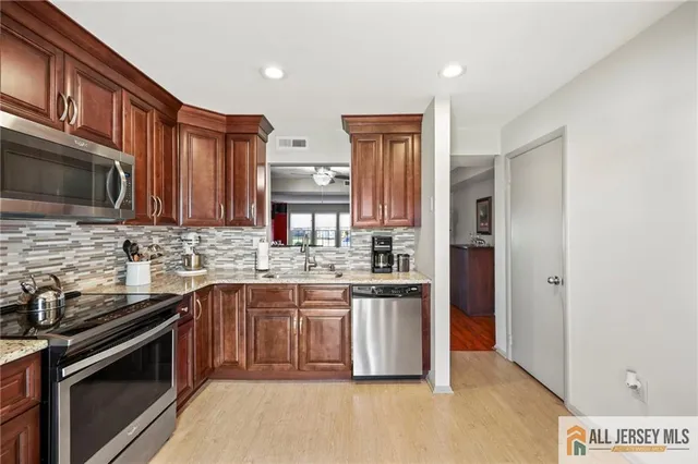 a kitchen with stainless steel appliances granite countertop a stove top oven a sink dishwasher and a refrigerator with wooden cabinets