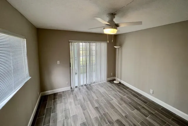 an empty room with wooden floor fan and windows