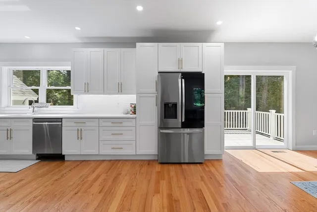 a kitchen with stainless steel appliances a stove top oven a refrigerator a sink and white cabinets with wooden floor