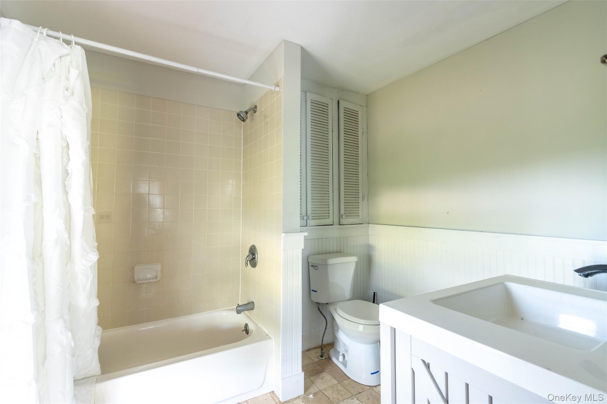 19450 Main Road Mattituck, NY 11952 - Photo 14 of 16 Full bathroom with shower / tub combo, vanity, wainscoting, light tile patterned flooring, and a closet