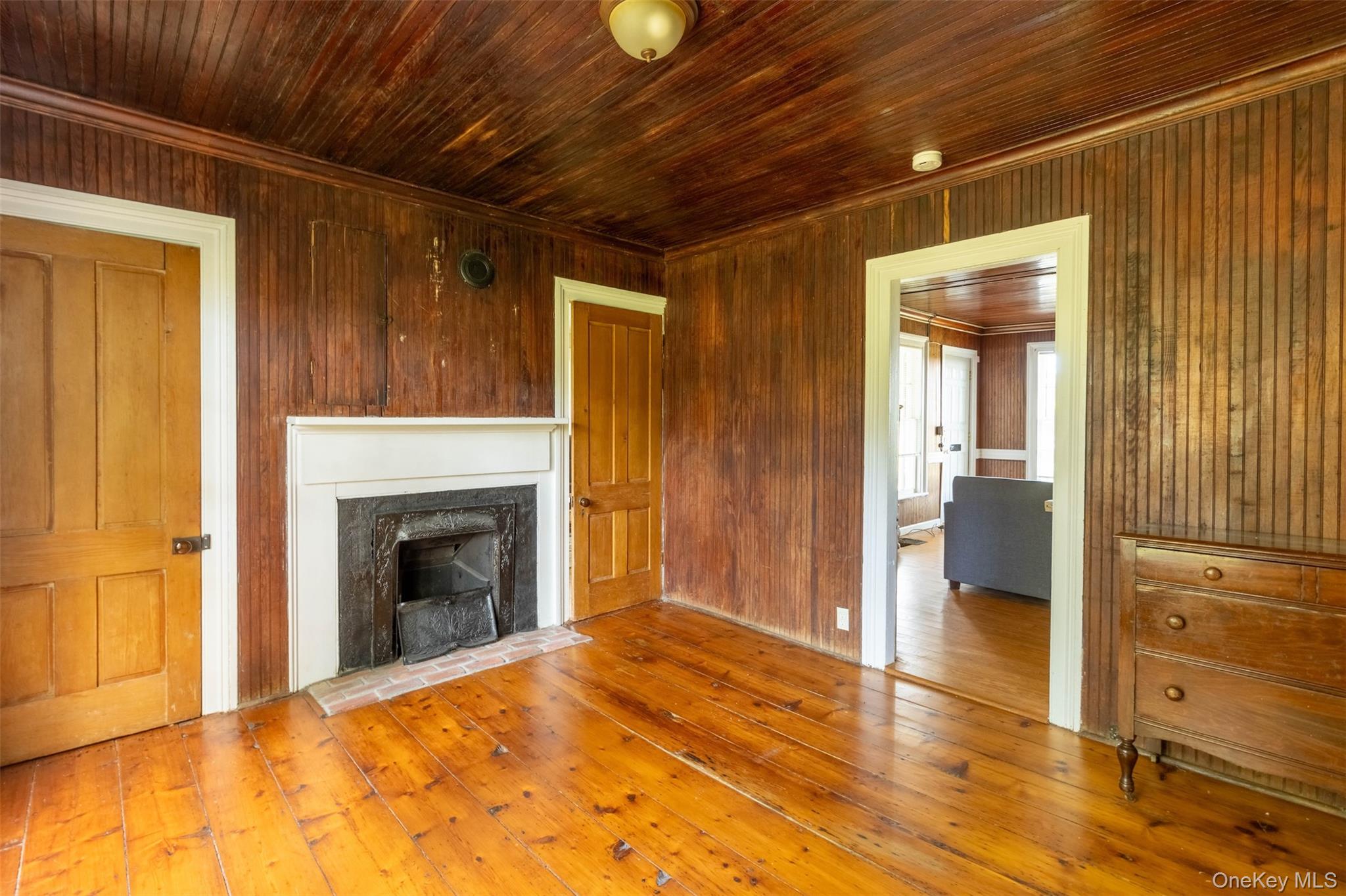 19450 Main Road Mattituck, NY 11952 - Photo 9 of 16 Unfurnished living room featuring hardwood / wood-style flooring, a fireplace, wood ceiling, crown molding, and wood walls