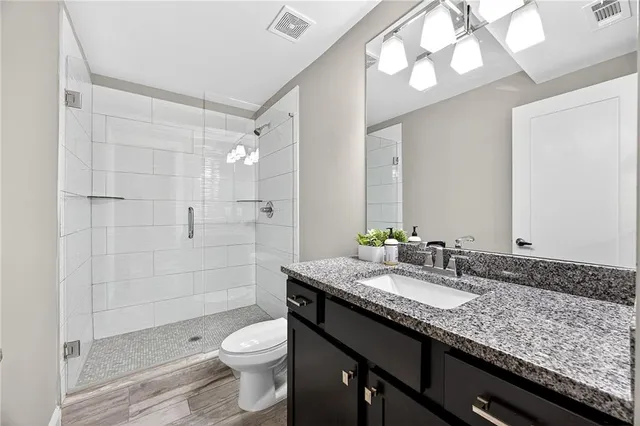 a bathroom with a granite countertop sink a toilet a mirror and shower