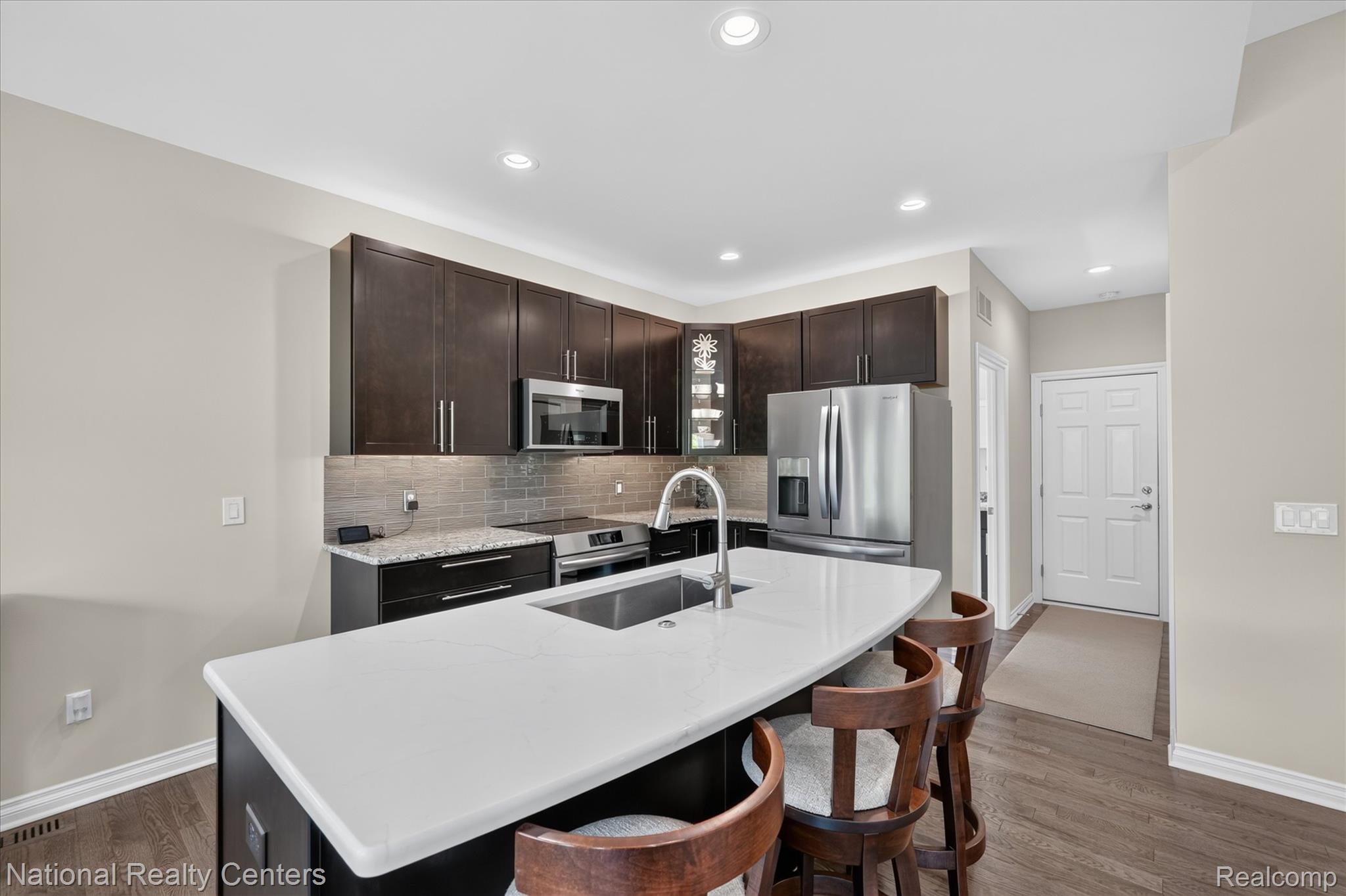 740 North Mill Street South Lyon, MI 48178 - Photo 21 of 56 Kitchen featuring a center island with a white countertop, dark wood-finish cabinetry, stainless steel appliances, a tile backsplash, and recessed lighting