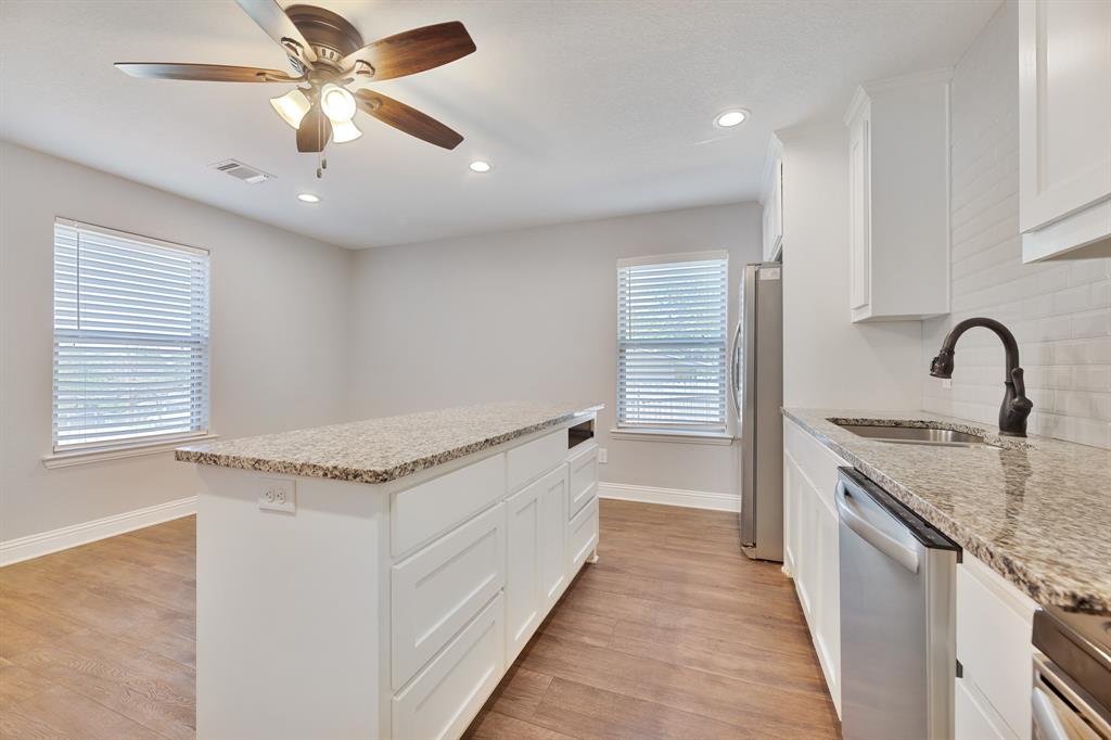1713 Bronco Road Granbury, TX 76049 - Photo 3 of 23 Kitchen featuring a central island with a granite countertop, white cabinetry, wood-finish flooring, a stainless steel dishwasher, and a black gooseneck faucet