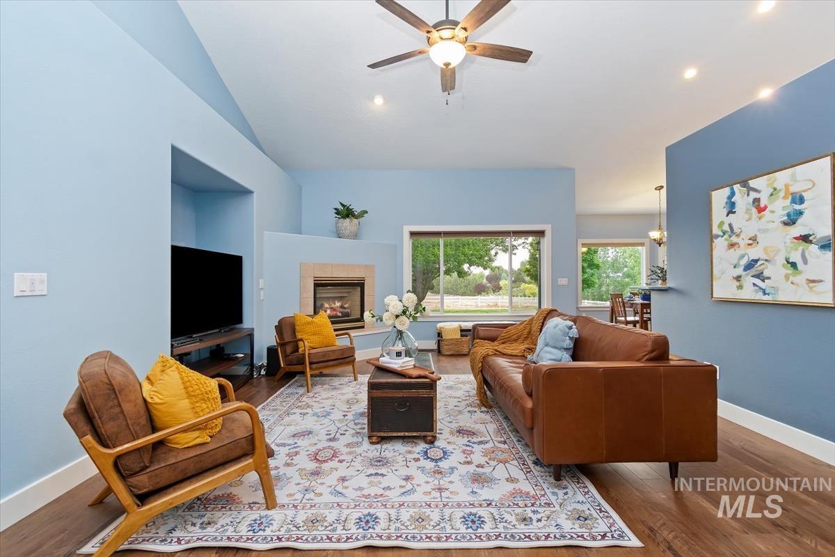 10462 West Lanktree Gulch Road Star, ID 83669 - Photo 5 of 48 Vaulted ceiling living area featuring a fireplace with a light-toned surround, a built-in media niche, a ceiling fan with integrated lighting, and wood-finish flooring