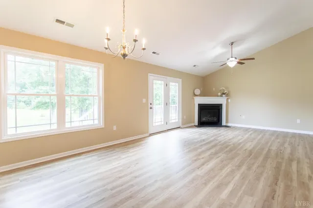 an empty room with wooden floor chandelier and windows