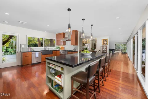 a kitchen with stainless steel appliances granite countertop a refrigerator a sink dishwasher a stove and a dining table with wooden floor