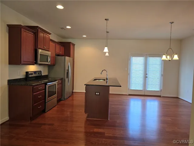 a kitchen with stainless steel appliances granite countertop a refrigerator a sink dishwasher a stove and a wooden floor