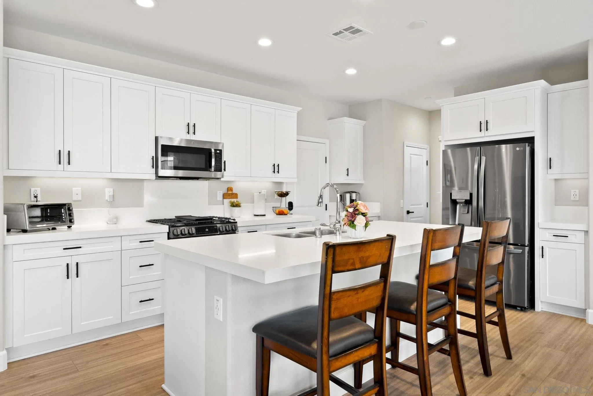 1279 Camino Prado Chula Vista, CA 91913 - Photo 7 of 38 a kitchen with stainless steel appliances a stove a sink a refrigerator and white cabinets with wooden floor