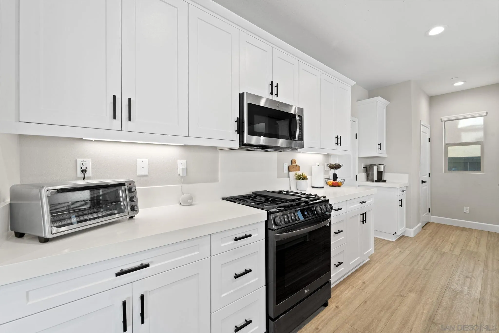 1279 Camino Prado Chula Vista, CA 91913 - Photo 9 of 38 a kitchen with stainless steel appliances granite countertop white cabinets a sink a stove a microwave and wooden floors