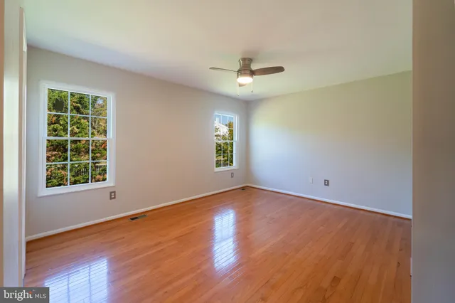 an empty room with wooden floor chandelier fan and windows
