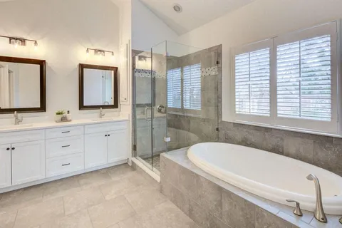 a bathroom with a tub a double vanity sink a window a mirror and a shower