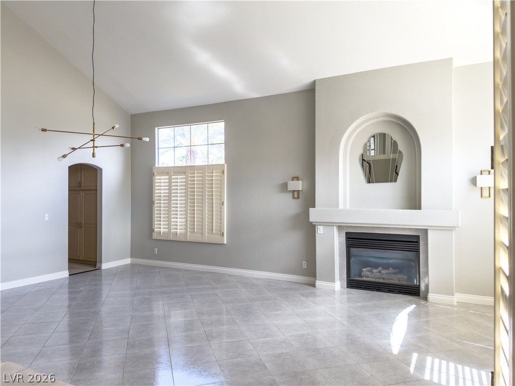 1842 Bogey Way Henderson, NV 89074 - Photo 2 of 25 Unfurnished living room with a tiled fireplace, vaulted ceiling, suspended lighting, arched walkways, and light tile patterned floors