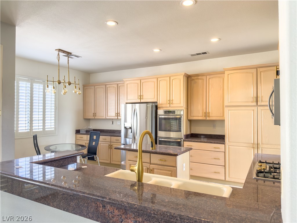 1842 Bogey Way Henderson, NV 89074 - Photo 4 of 25 Kitchen with stainless steel appliances, light wood finish cabinets, a kitchen island, and a chandelier