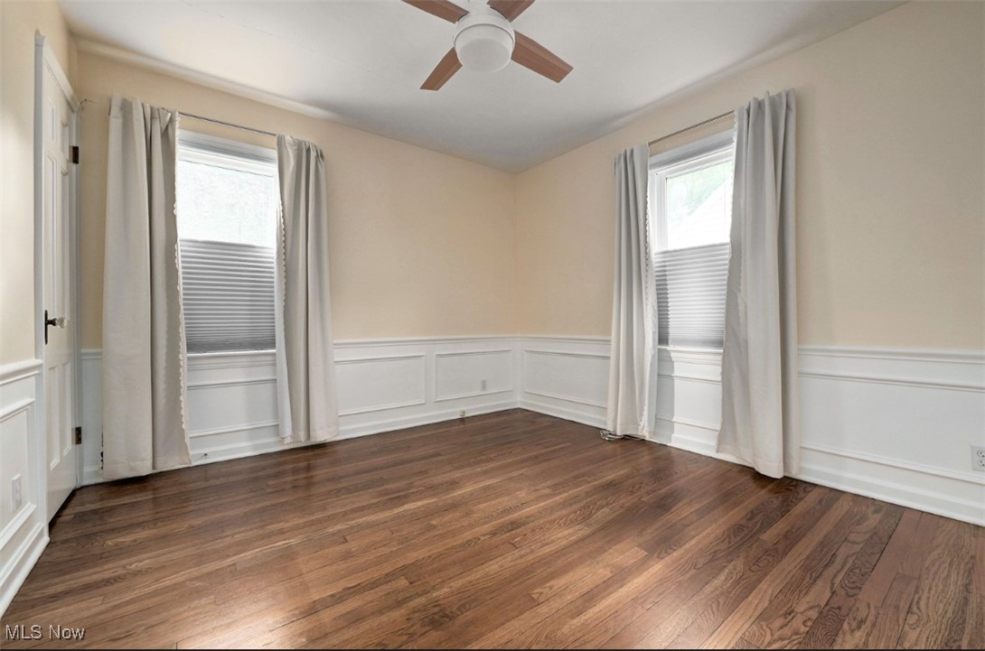 16501 Munn Road Cleveland, OH 44111 - Photo 8 of 42 Empty room with a ceiling fan, dark wood-style floors, a wainscoted wall, and a decorative wall