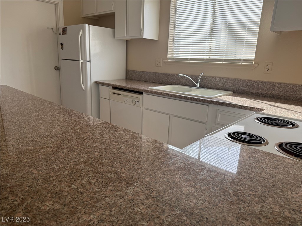 4689 West Sand Creek Avenue, Unit C Las Vegas, NV 89103 - Photo 5 of 14 Kitchen with dark countertops, white cabinets, and white appliances